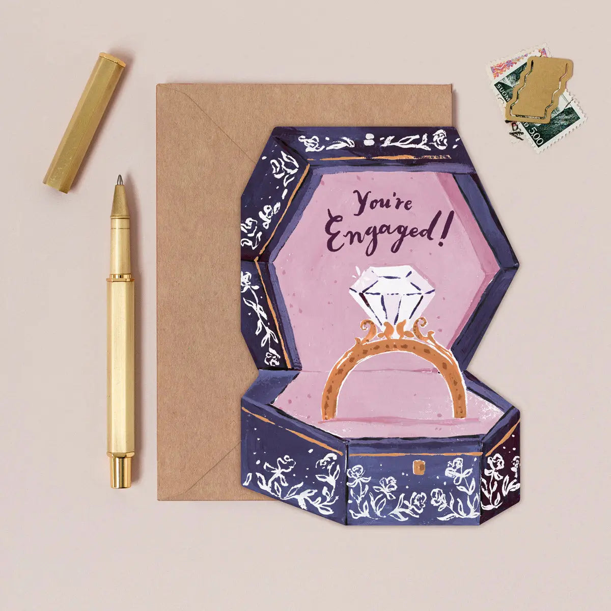 Glückwunschkarte zur Verlobung "You're engaged!" mit illustrierter Ringbox und Diamantring auf Kraftpapier-Umschlag