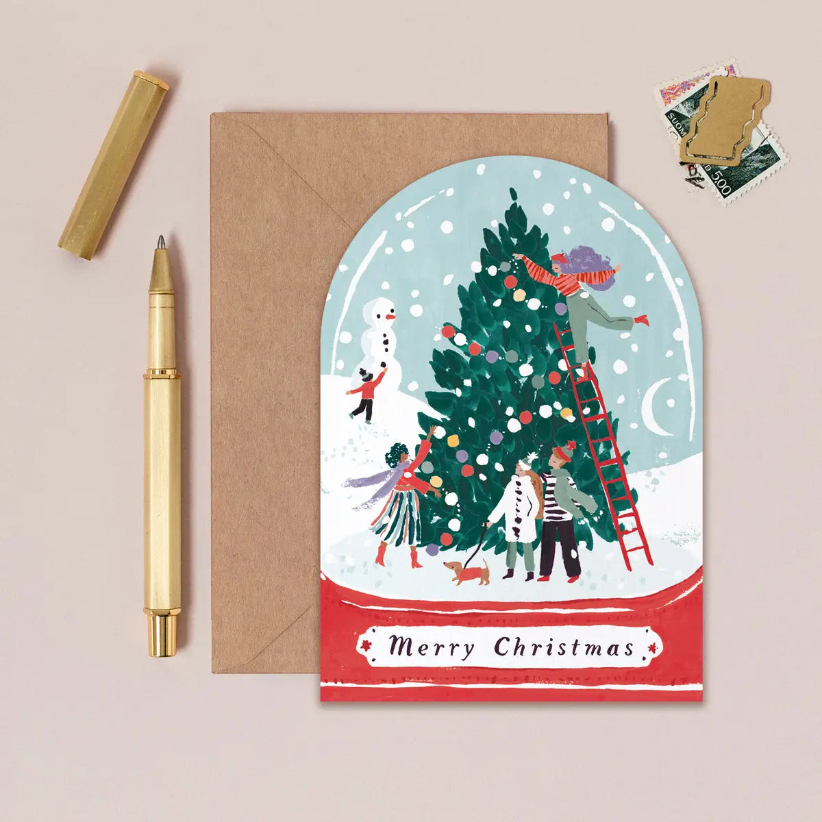 Weihnachtskarte in Schneekugel-Form mit geschmücktem Tannenbaum, Schneemann und "Merry Christmas" auf Kraftpapier-Umschlag