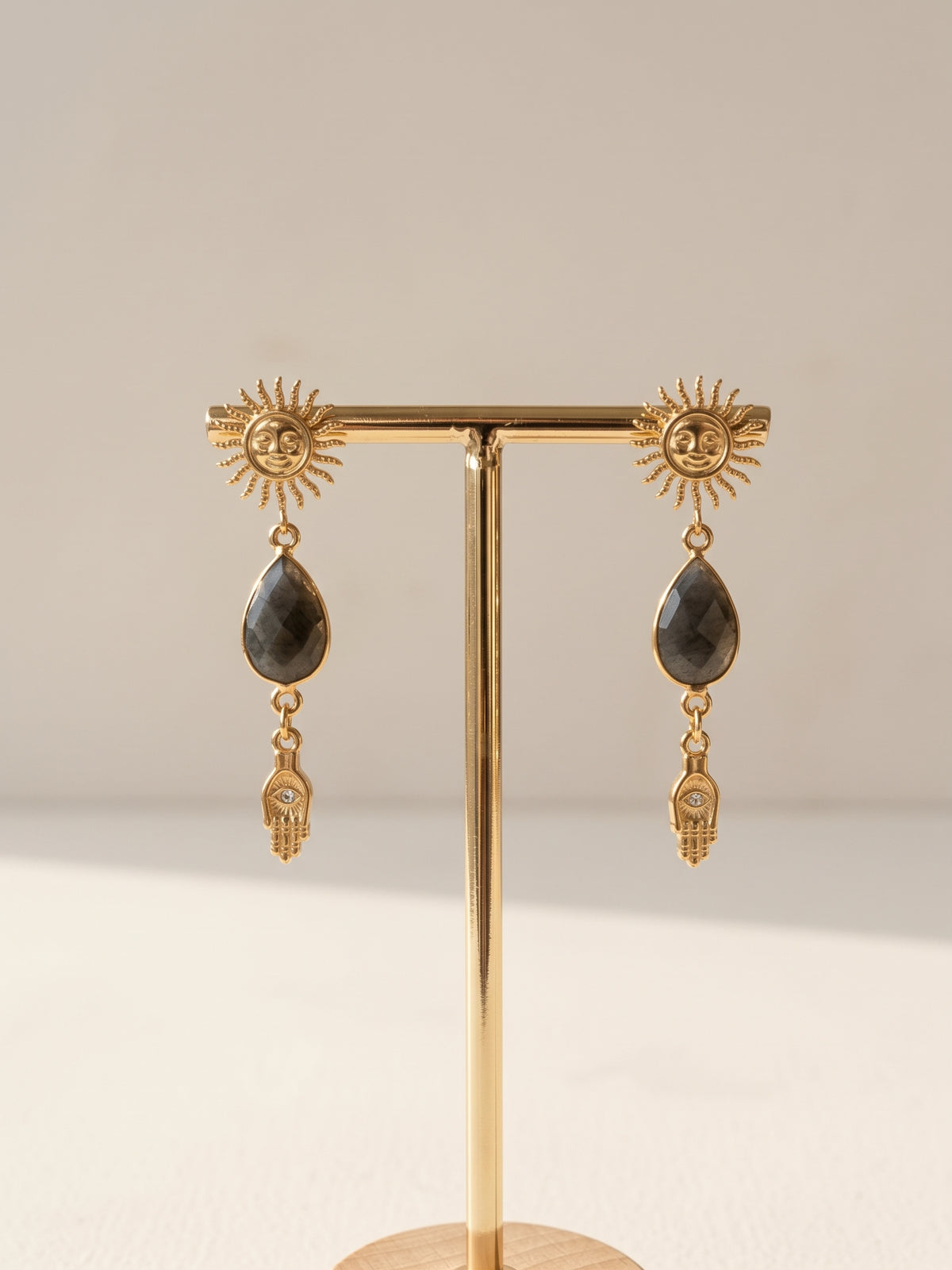 Handgefertigte Ohrringe mit Sonnen-Stecker, Labradorit-Tropfen und Hamsa-Hand mit Zirkonia, goldfarben, an einem Schmuckständer
